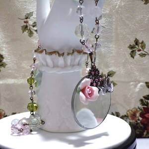 Peut inclure: Un collier de style vintage avec un pendentif en forme de loupe. Le pendentif est orn&eacute; d'une fleur rose et de strass. Le collier est compos&eacute; de perles de verre transparentes et vertes.