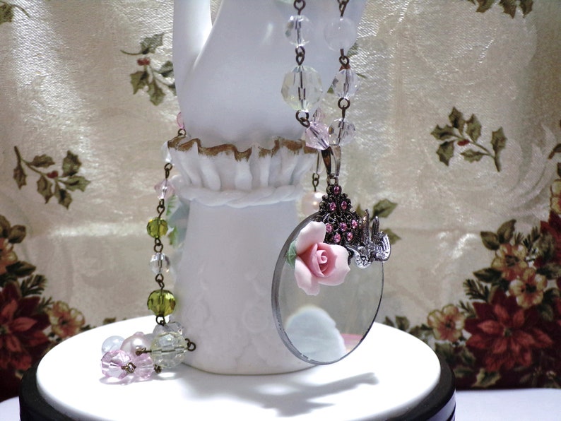 Peut inclure: Un collier de style vintage avec un pendentif en forme de loupe. Le pendentif est orn&eacute; d'une fleur rose et de strass. Le collier est compos&eacute; de perles de verre transparentes et vertes.