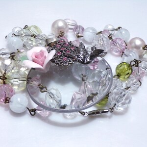 Peut inclure: Un collier d&eacute;licat avec un pendentif en verre transparent, orn&eacute; d'une fleur rose et d'un charme d'oiseau argent&eacute;. Le collier est compos&eacute; de perles de verre transparentes, roses et vertes.