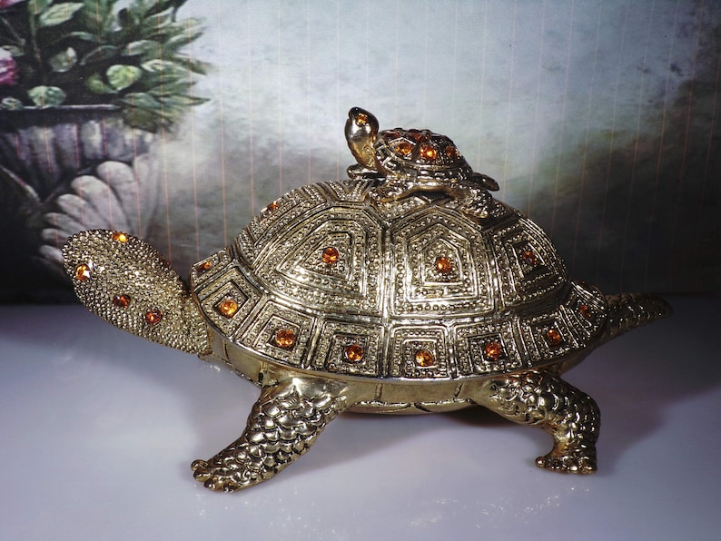 May include: A gold-colored turtle figurine with a smaller turtle on its back. Both turtles are decorated with orange rhinestones.