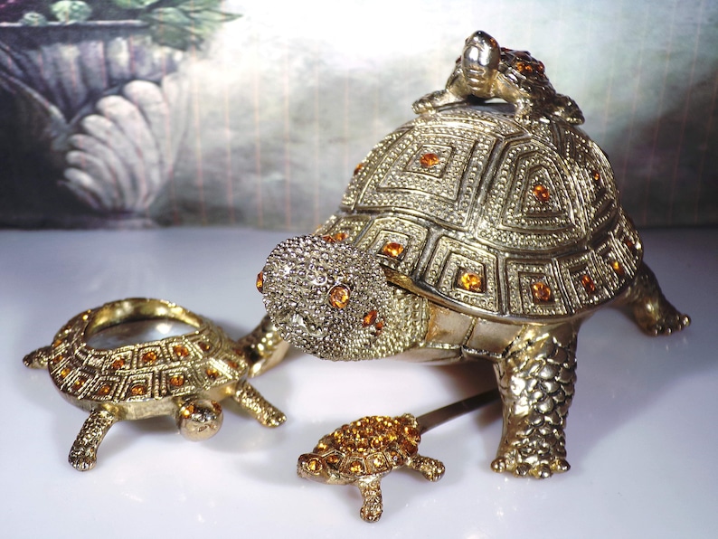 May include: Three gold-tone turtle figurines with amber-colored rhinestones. The largest turtle has a smaller turtle on its back.