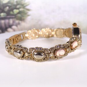 May include: Gold-toned bracelet watch with oval and cameo-style accents. The watch features a decorative link design with a clasp closure. The watch face is rectangular and has a gold-tone finish. The bracelet is approximately 7 inches in length.