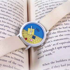 May include: A Cheval Quartz wristwatch with a white case and a textured off-white strap. The watch face features a blue and yellow grid pattern with small red, pink, and blue squares, white hands, and the text Cheval Quartz printed on the dial.