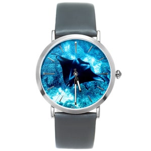 May include: A silver wristwatch with a grey leather strap. The watch face features a blue and white image of a manta ray swimming in the ocean.