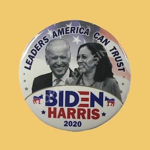 May include: A white button with a blue and red design. It features a photo of Joe Biden and Kamala Harris with the text "Leaders America Can Trust" and "Biden Harris 2020".