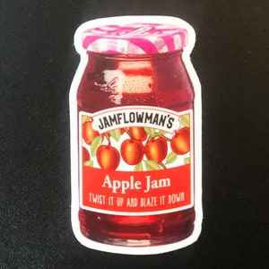 May include: A sticker of a red glass jar of apple jam with a white label that says "JAMFLOWMAN'S Apple Jam Twist it up and blaze it down". The jar has a pink and white lid and is surrounded by red apples.