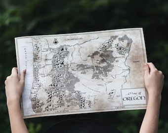 Könnte beinhalten: Eine Person hält eine Vintage-Karte von Oregon, mit dem Text "Map of Oregon" in einem Kasten unten rechts. Die Karte ist auf gealtertem Papier gedruckt und zeigt die wichtigsten Städte, Flüsse und Berge des Bundesstaates.
