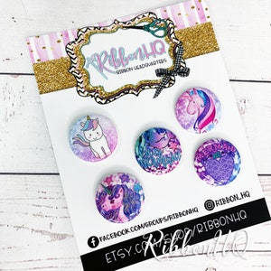 Puede incluir: Cuatro botones de 2,5 cm de diámetro con diseños de unicornio, sirena y texto "Sea Mermaid". Los botones están en una tarjeta blanca con el texto "Ribbon HQ" y los identificadores de las redes sociales.