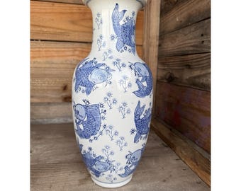 May include: A white ceramic vase with a flared top and a wide base. The vase is decorated with blue koi fish and floral patterns. The vase is approximately 30 cm tall.