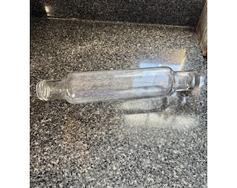 May include: A clear glass rolling pin with a hollow cylindrical body and two distinct handle ends. The rolling pin features a smooth, transparent surface and a threaded neck design on one side, indicating it is a refillable glass kitchen tool.