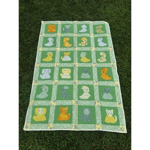 May include: A rectangular quilt featuring a grid of green fabric squares, each containing an appliqued animal figure in various colors and patterns. The quilt is bordered by a white edge and includes small yellow floral squares at the corners.