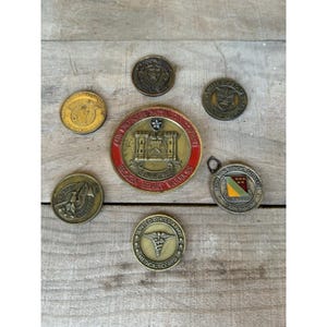 May include: A collection of vintage military challenge coins and medallions. The coins feature various designs, including the United States Army Medical Corps emblem, a castle, and the text "Broken Heart Warriors."