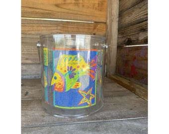 May include: A clear, cylindrical ice bucket with a colorful fish design. The fish is yellow, green, and orange, with a blue background and a starfish. The bucket has metal handles.