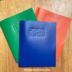 May include: Three personalised binders in green, blue and orange with the name "Grayson" embroidered on each.