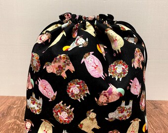 May include: Black drawstring bag with a floral sheep pattern. The sheep are wearing flower crowns and some are holding yarn.