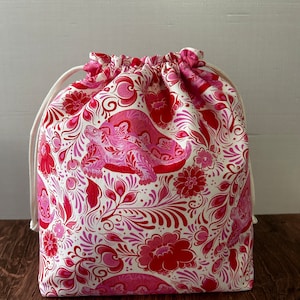 May include: A white drawstring bag with a pink and red floral pattern. The pattern features stylized flowers, leaves, and a turtle.