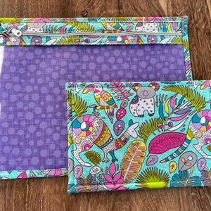 Puede incluir: Dos bolsas de tela con un estampado tropical colorido con tucanes, koalas y otros animales. La bolsa m&aacute;s grande tiene una ventana transparente y cierre de cremallera. La bolsa m&aacute;s peque&ntilde;a es rectangular.