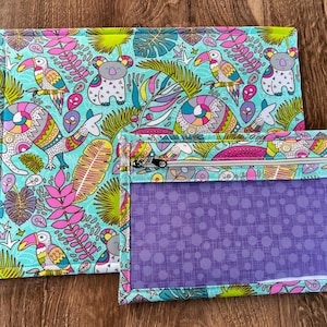 Puede incluir: Dos bolsas de tela con un colorido estampado tropical con tucanes, koalas y otros animales. La bolsa m&aacute;s grande es rectangular, y la m&aacute;s peque&ntilde;a tiene una ventana p&uacute;rpura transparente y una cremallera.
