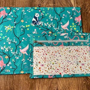 May include: Two teal blue fabric placemats with a floral and animal print. The smaller placemat has a clear plastic window and a zipper.