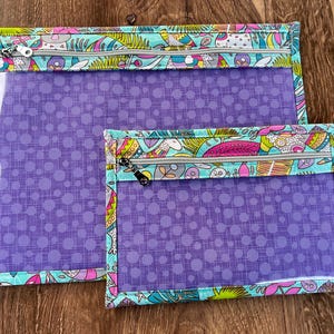 Puede incluir: Dos bolsas con cremallera, una grande y otra peque&ntilde;a, con frente transparente y un estampado de lunares morados. Los bordes est&aacute;n ribeteados con una tela colorida con dise&ntilde;os caprichosos y un fondo turquesa. Las cremalleras son plateadas.