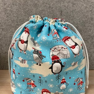 May include: A blue drawstring bag with a penguin and snowflake pattern. The bag is made of fabric and has a white drawstring.