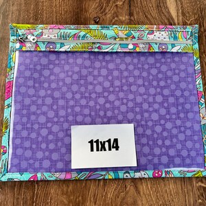 Puede incluir: Una bolsa rectangular con cremallera, con frente transparente y un patr&oacute;n de puntos morados. La bolsa est&aacute; bordeada con una tela estampada colorida con p&aacute;jaros y flores. Una etiqueta blanca con "11x14" est&aacute; en el frente.