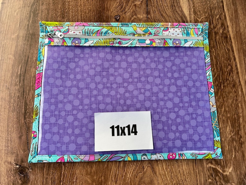 Puede incluir: Una bolsa rectangular con cremallera, con frente transparente y un patr&oacute;n de puntos morados. La bolsa est&aacute; bordeada con una tela estampada colorida con p&aacute;jaros y flores. Una etiqueta blanca con "11x14" est&aacute; en el frente.