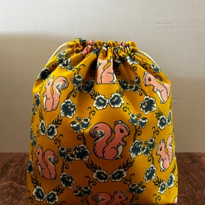 May include: A yellow drawstring bag with a pink squirrel and floral pattern.