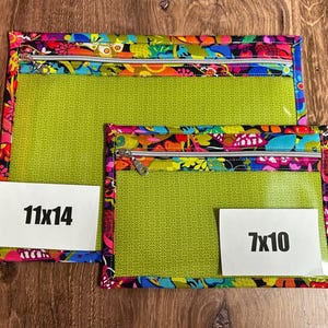 Puede incluir: Dos bolsas transparentes con cremallera y ribete floral colorido. La bolsa m&aacute;s grande mide 28x36 cm, y la m&aacute;s peque&ntilde;a mide 18x25 cm. Ambas tienen un interior verde y una cremallera blanca.