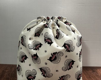 May include: A white drawstring bag with a pattern of black squirrels with pink accents. The bag is made of a soft, fabric material.