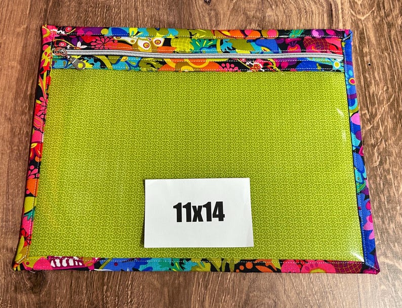 Puede incluir: Bolsa rectangular con un borde floral colorido y una cremallera plateada. El centro es verde lima y transparente. Una etiqueta blanca muestra "11x14".