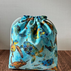 May include: A blue drawstring bag with a pattern of colorful sea turtles. The bag is made of fabric and has a white drawstring.
