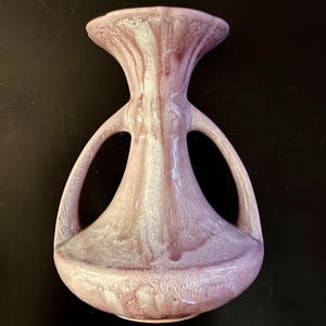 May include: A pink and white ceramic vase with two handles. The vase has a textured surface and a unique shape.