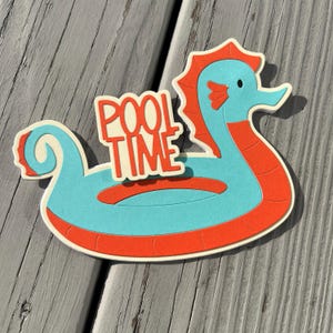 May include: A light blue and orange paper cutout of a seahorse pool float with the words "Pool Time" on it.