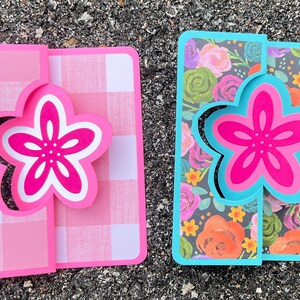 May include: Two handmade greeting cards with a pop-up flower design. The card on the left has a pink and white gingham pattern. The card on the right has a floral pattern with pink, orange, yellow, and green flowers on a black background.