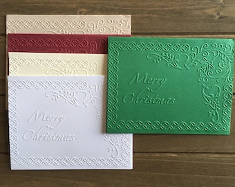 May include: Set of five blank greeting cards with an embossed border and the text "Merry Christmas". The cards are in various colors, including white, cream, red, and green.