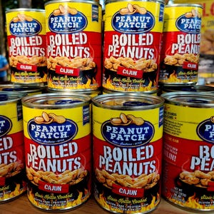 Könnte beinhalten: Ein Stapel Dosen mit gekochten Erdnüssen der Marke "Peanut Patch". Die Dosen haben ein gelb-rotes Farbschema mit dem Schriftzug "Boiled Peanuts" in großen weißen Buchstaben. Die Sorte "Cajun" ist hervorgehoben.