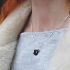 A small black onyx crystal necklace on a model’s neck.