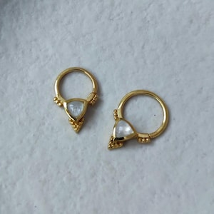May include: A pair of gold hoop earrings with a triangular white gemstone in the centre of each hoop. The hoops are decorated with small gold beads.