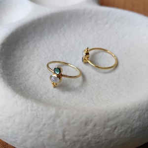 Pode incluir: Duas alianças de ouro com pedras brancas e verdes. As alianças estão em um prato de cerâmica branco.