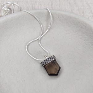 A silver necklace with a smokey quartz pendant, adorned with dotted details.