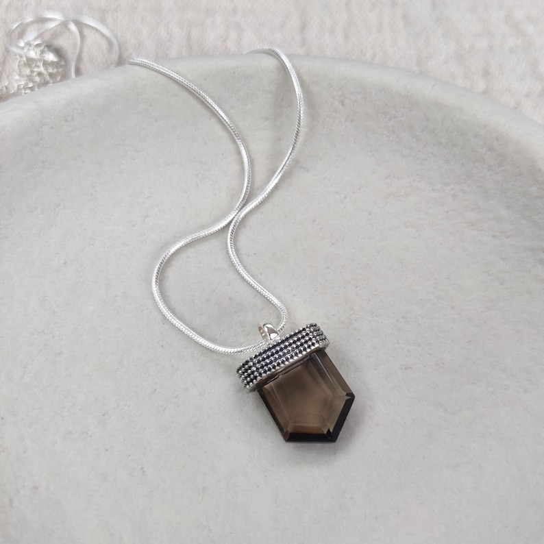 A silver necklace with a smokey quartz pendant, adorned with dotted details.