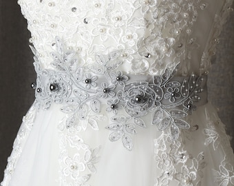 May include: A white lace wedding dress with a silver beaded and floral lace sash.
