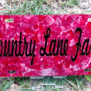 May include: A red and white marbled license plate with black lettering that reads "Country Lane Farms".