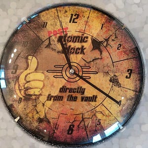 May include: A round, yellow, and brown clock with a cracked, distressed look. The clock face has black hands and black numbers. The clock face also has the text "Post Atomic Clock" and "directly from the vault".