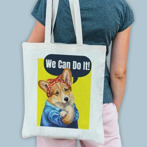 May include: A white tote bag with a yellow background and a cartoon image of a corgi wearing a blue shirt and a red bandana. The corgi has its arm raised in a fist with the words "We Can Do It!" in a speech bubble above the corgi.
