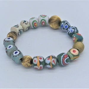 Puede incluir: Un brazalete hecho de cuentas de vidrio de colores con acentos blancos, verdes, azules y rojos. Las cuentas están enhebradas en un cordón dorado.