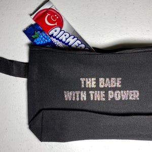 May include: Black canvas zippered pouch with the text "THE BABE WITH THE POWER" in glitter lettering. The pouch contains two Airheads candy bars, one red and one blue.