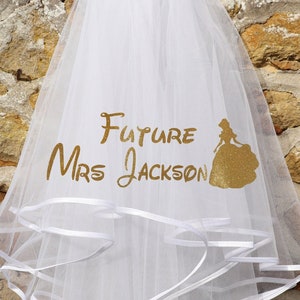 May include: A white bridal veil with multiple layers and a cascading design. The veil features the text "Future Mrs Jackson" in gold lettering, along with a gold silhouette of a bride. White ribbon trim adds detail.