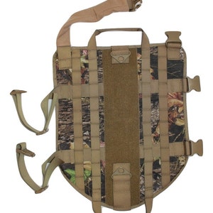 May include: A camouflage dog harness with adjustable straps and buckles. The harness has a handle on the top and a D-ring on the side.